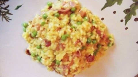 Ein gelbes Risotto Milanese wird auf einem dekorativen Teller serviert, umgeben von frischen Kräutern und Gemüse.