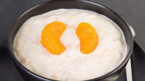 Ein schwarzes Schüsselchen enthält ein cremiges Schütteldessert, dekoriert mit Mandarinen, auf einem dunklen Untergrund.