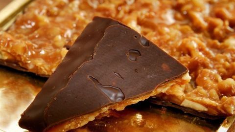 Eine goldene Florentiner-Süßigkeit liegt auf einem Blech, umgeben von weiteren knusprigen Stücken, die appetitlich aussehen.