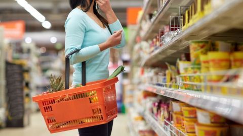 Eine Frau steht in einem Supermarkt und hält einen Einkaufskorb, während sie die Regale mit Lebensmitteln betrachtet.