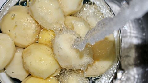 Kartoffeln werden in einer Schüssel unter fließendem Wasser gereinigt, während sie gleichzeitig garen, um Strom zu sparen.