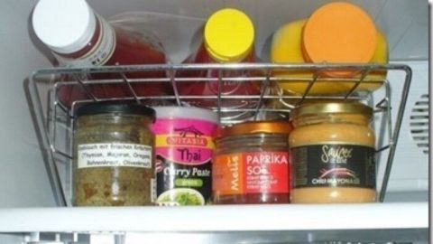 Ein Kühlschrank mit mehreren Regalen zeigt سامان in ordentlich angeordneten Gläsern und Flaschen für bessere Ordnung.