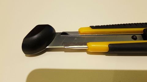 Ein Cuttermesser mit gelben Griffen liegt auf einer neutralen Oberfläche, bereit, um die Klingen sicher abzubrechen.