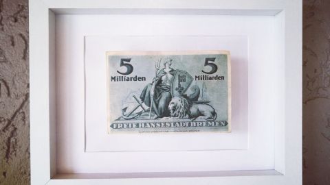 Ein gerahmter Geldschein im weißen Rahmen dekoriert eine raue Wand. Diese günstige Wanddekoration ist ansprechend platziert.