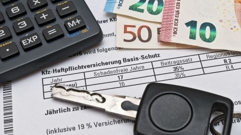 Ein Schlüssel und eine Geldbörse liegen auf einem Versicherungsvertrag, während ein Taschenrechner daneben steht.
