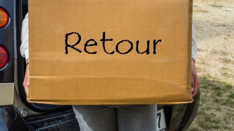 Eine Person trägt einen Karton mit der Aufschrift "Retour", während sie neben einem Fahrzeug steht und Rücksendegebühren anzeigt.
