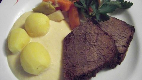 Zarte Scheiben Tafelspitz liegen neben cremiger Meerrettichsoße und Beilagen wie Kartoffeln und buntem Gemüse angerichtet.