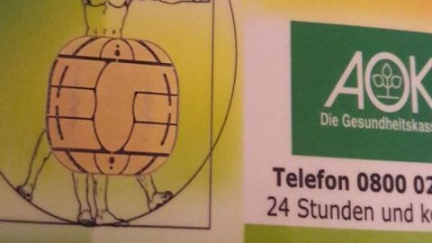 Eine Gesundheitskarte zeigt das AOK-Logo und eine Illustration eines menschlichen Körpers im Kreis, umrahmt von grünem Hintergrund.
