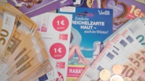 Eine Vielzahl von Geldscheinen, Münzen und Coupons liegt auf einer Oberfläche, die den Akt des Sparens verdeutlicht.
