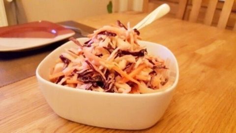 Cremiger Krautsalat befindet sich in einer weißen Schüssel auf einem Holztisch und sieht frisch zubereitet aus.