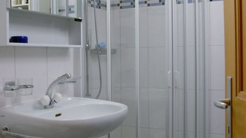 Eine Duschkabine steht in einem hellen Badezimmer mit weißen Fliesen, während das Waschbecken für die Reinigung genutzt wird.