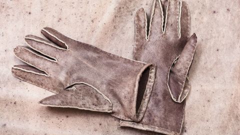 Leder-Fingerhandschuhe mit kaputtem Futter liegen auf einem hellen, strukturierten Untergrund und scheinen genutzt zu sein.