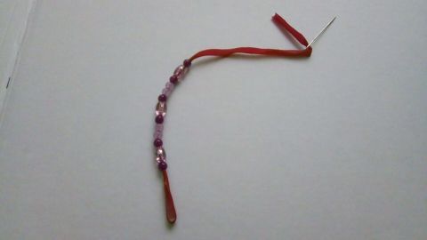 Ein rotes Gummiband mit bunten Perlen ist zu einem Armband geflochten, auf einem weißen Untergrund liegend.