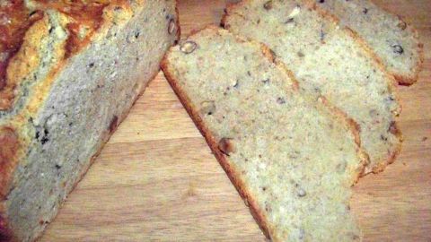 Ein frisch gebackenes Buttermilchbrot mit Nüssen liegt auf einem Holzbrett, mit mehreren geschnittenen Scheiben daneben.