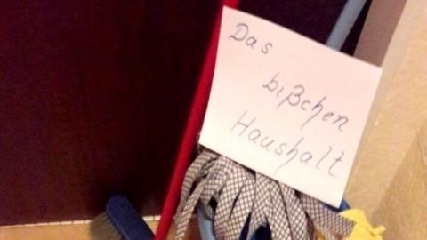 Besen und Wischmob liegen zusammen auf dem Boden, während ein Schild mit „Das bisschen Haushalt“ darüber hängt.