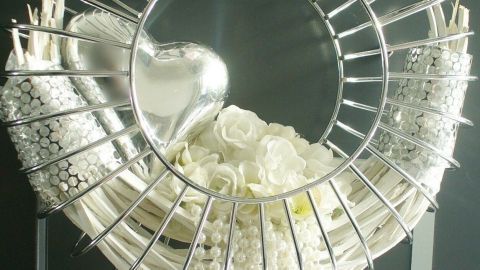 Ein moderner Türkranz aus einem ehemaligen Adventskranz hängt an einer Wand und ist mit weißen Blumen und Perlen verziert.