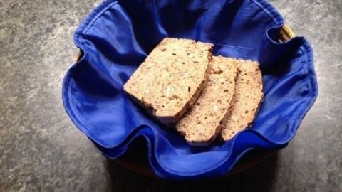 Körndlbrot liegt in einem blauen Brotkorb, während es auf einer dunklen Fläche präsentiert wird.