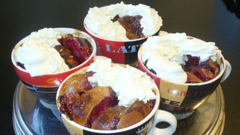 Sechs Tassenkuchen aus Berlinern in bunten Tassen, gefüllt mit fruchtiger Füllung und bedeckt mit Sahne, stehen auf einem Tablett.