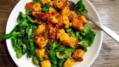 Die Feldsalat-Porte präsentiert frischen, grünen Feldsalat, garniert mit knusprigen, gerösteten Linsenbrotstücken.