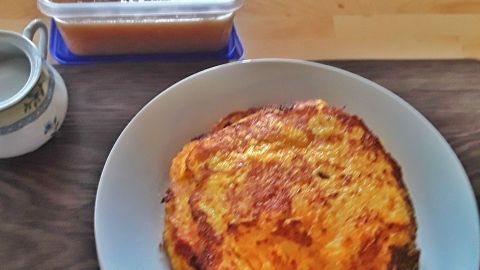 Goldbraune Kartoffelpuffer liegen auf einem Teller, daneben eine Schüssel mit Apfelmus und eine kleine Kanne.
