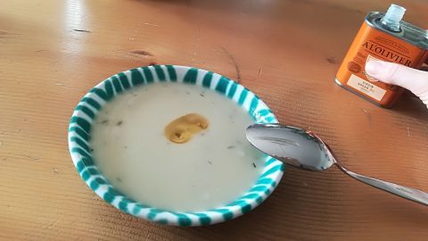 Eine Schüssel mit Topinambur-Cremesuppe steht auf einem Holztisch, während ein Löffel daneben liegt.