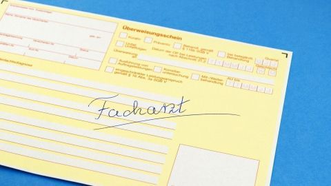 Ein gelbes Dokument zeigt den Schriftzug „Facharzt“ und enthält Platz für Informationen zu einem Arzttermin. Es liegt auf einem blauen Hintergrund.