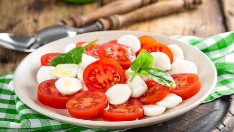 Frischer Tomate-Mozzarella-Teller liegt auf einem Holztisch, umgeben von Kräutern und Olivenöl in einer rustikalen Küche.
