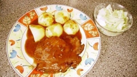 Saftiger marinierter Schweinebraten liegt auf einem bunt dekorierten Teller, umgeben von Kartoffeln und Weißkrautsalat.