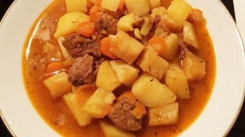 Ein ungarischer Kesselgulasch besteht aus zarten Fleischstücken, Kartoffeln und Gemüse in einer würzigen, roten Sauce, appetitlich angerichtet auf einem weißen Teller.