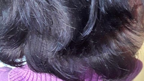 Dunkles, gesundes Haar in einem sanften Schwung fällt über den Nacken, getragen von einem lila Rollkragenpullover.