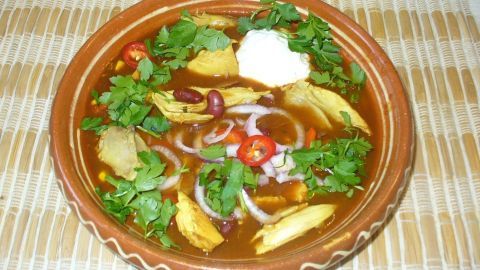 Eine dampfende Schüssel Tex-Mex-Hühnersuppe mit frischen Kräutern und Zutaten, serviert auf einem gedeckten Tisch.