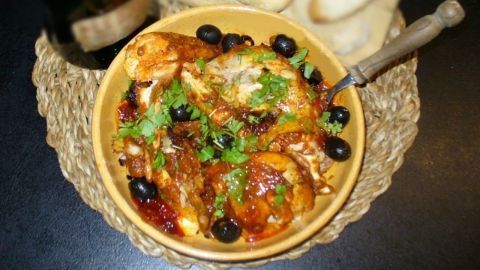 Ein köstliches Oliven-Sherry-Hähnchen in einer gelben Schüssel, umgeben von frischem Brot und einer Flasche Wein.