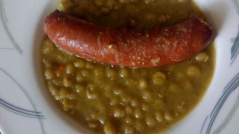 Ein Teller mit Erbseneintopf zeigt grüne Erbsen und eine Bratwurst, appetitlich angerichtet auf einem weißen Teller.