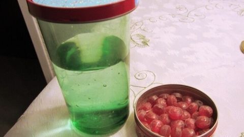 Ein grünes Trinkglas steht neben einer Dose mit roten Beeren. Das Glas scheint abgedeckt zu sein, um Insekten fernzuhalten.
