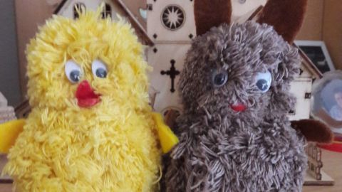 Ein gelbes Küken und ein braunes Häschen mit großen Augen stehen auf einem Tisch, dekorativ für Ostern.