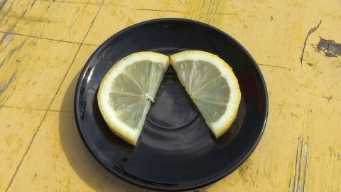 Zwei Zitronenscheiben liegen auf einem schwarzen Teller, umgeben von einer hellgelben Tischfläche, um das Trinken von Wodka zu begleiten.