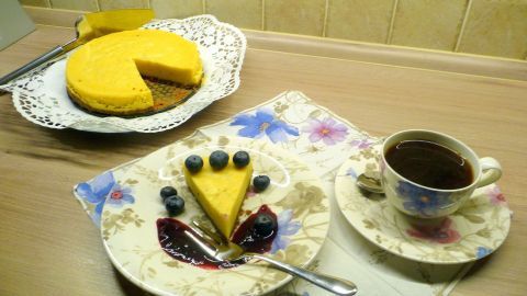 Ein Käsekuchen aus dem Schnellkochtopf steht auf einem Teller, neben einer Tasse Kaffee auf einem blumigen Tischset.