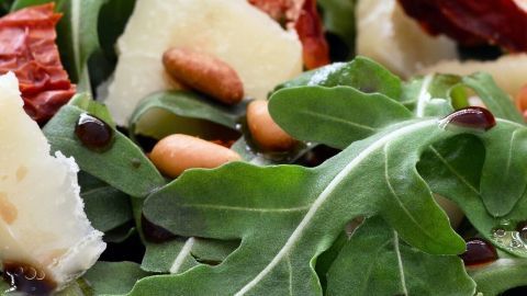 Ein frischer Salat mit Rucola, Sonnengetrockneten Tomaten und Feta-Käse wird in einer Schüssel angerichtet, bereit für die Balsamico-Ahornsirup-Salatsoße.