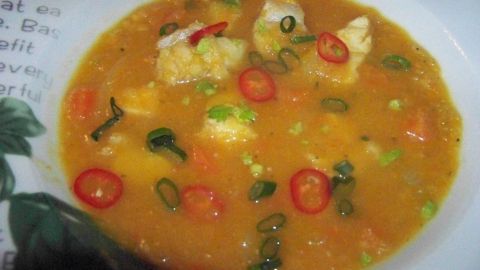 Eine schmackhafte Süßkartoffelsuppe mit mariniertem Fisch und frischen Kräutern in einer weißen Schale serviert.