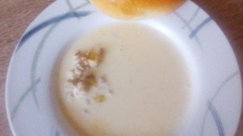 Eine Schüssel Käse-Lauch-Suppe steht auf einem Teller, daneben liegt ein halbierter Brötchen.