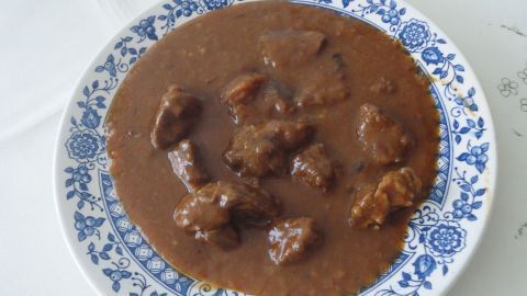 Ein Teller mit Saftgulasch zeigt zarte Fleischstücke in dicker, dunkler Sauce auf einem blauen, gemusterten Teller.