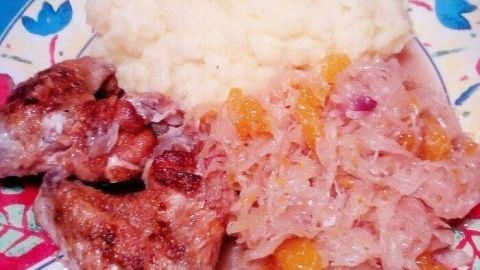 Saftiges Hähnchen auf Rebhuhnart liegt neben cremigem Püree und herzhaftem Sauerkraut mit Orangenscheiben.