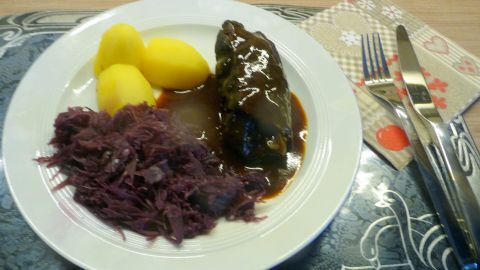 Zarte Rouladen liegen auf einem Teller, umgeben von Kartoffeln und Rotkohl, alles appetitlich angerichtet.