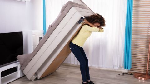 Eine Person hebt schweres Möbel, während sie in einem hellen Wohnzimmer steht, um es leicht zu verschieben.
