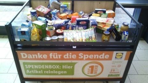 Eine Spendenbox, gefüllt mit Lebensmitteln, steht in einem Geschäft; "Danke für die Spende" ist gut sichtbar.