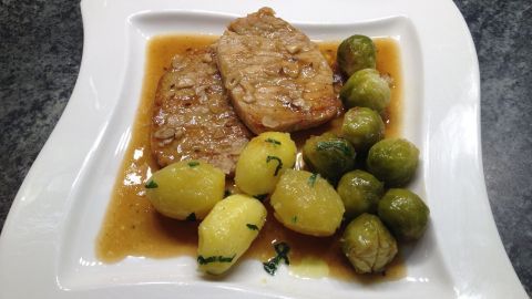 Zarte Karreeschnitzel liegen auf einem eleganten Teller, umgeben von knusprigen Brüsseler Sprossen und Kartoffeln in Soße.