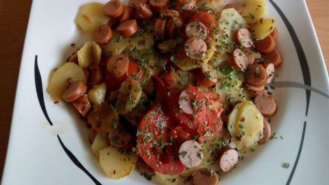 Eine Pfanne mit Kümmel-Kartoffel-Würstchen zeigt eine appetitliche Mischung aus Kartoffeln, Würstchen und Kräutern.