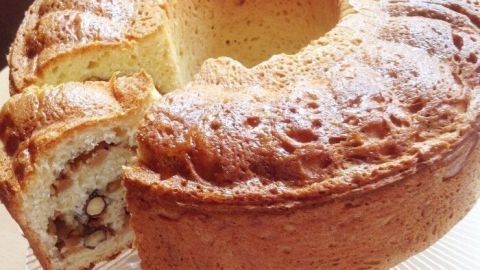 Ein Hefekranz aus Apfel und Nuss steht auf einem Kuchenteller, mit einem Stück herausgeschnitten, in einer hellen Küche.