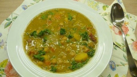 Ein Teller Kichererbsen-Eintopf steht auf einem blumigen Tischset, umgeben von einem Löffel, bereit zum Essen.