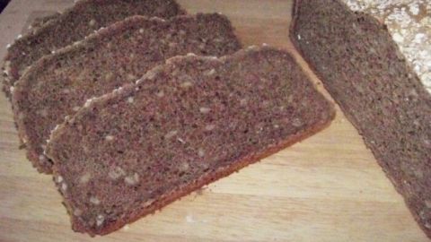 Dinkelvollkornbrot liegt auf einem Holzbrett, mit mehreren geschnittenen Scheiben, in einem rustikalen Küchenkontext.